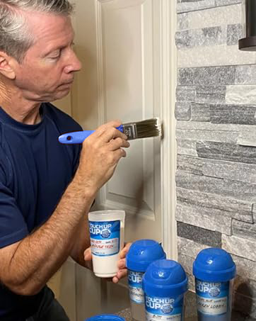 four Touch up cups and touch up brush being used to touch up pain on door frame by handy man